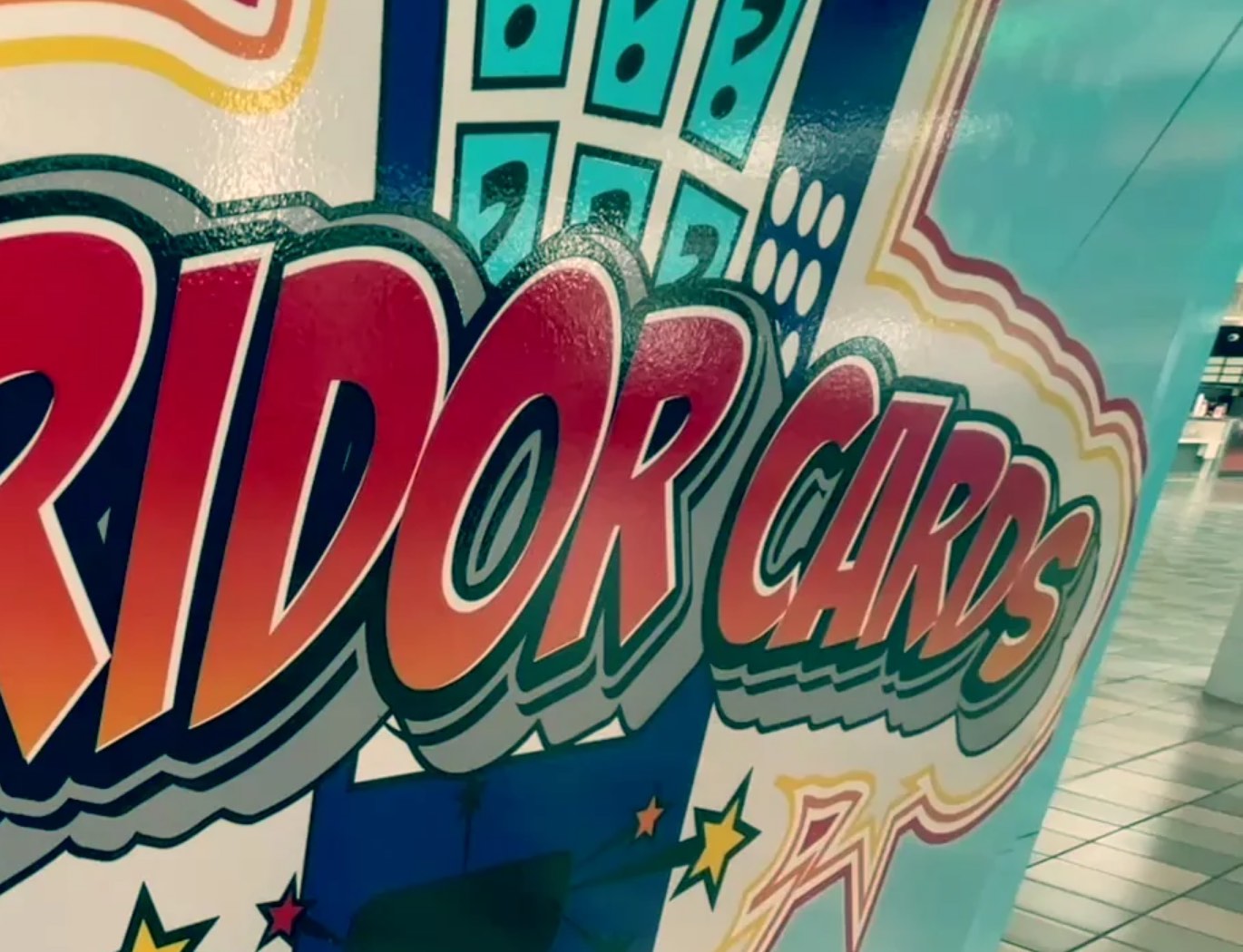 A Corridor Cards vending machine’s wrap: “Corridor Cards” in red and orange comic lettering beside a panel of teal question-mark tiles, with a tiled indoor floor behind the machine.